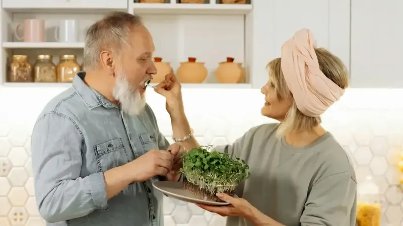 Older couple preparing and sharing a healthy meal of microgreens in their kitchen representing protein intake for seniors
