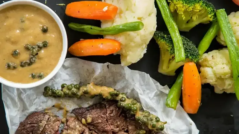 Sliced steak with colourful vegetables and sauce on a dark surface representing common protein foods and myths