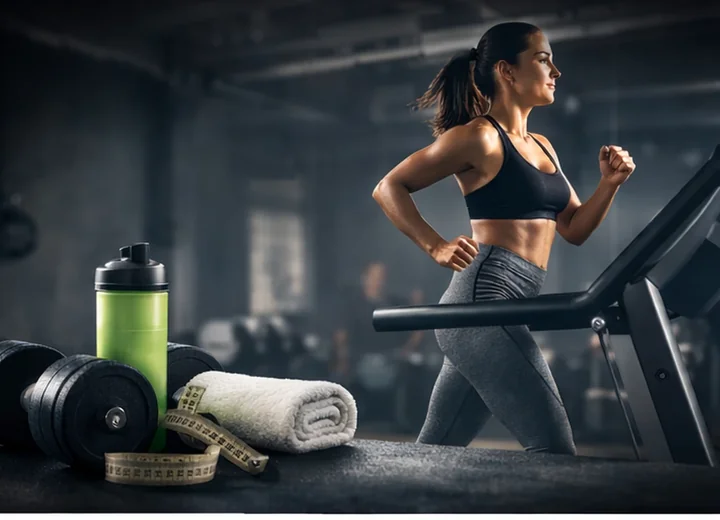 Woman running on a treadmill beside a shaker bottle and gym kit