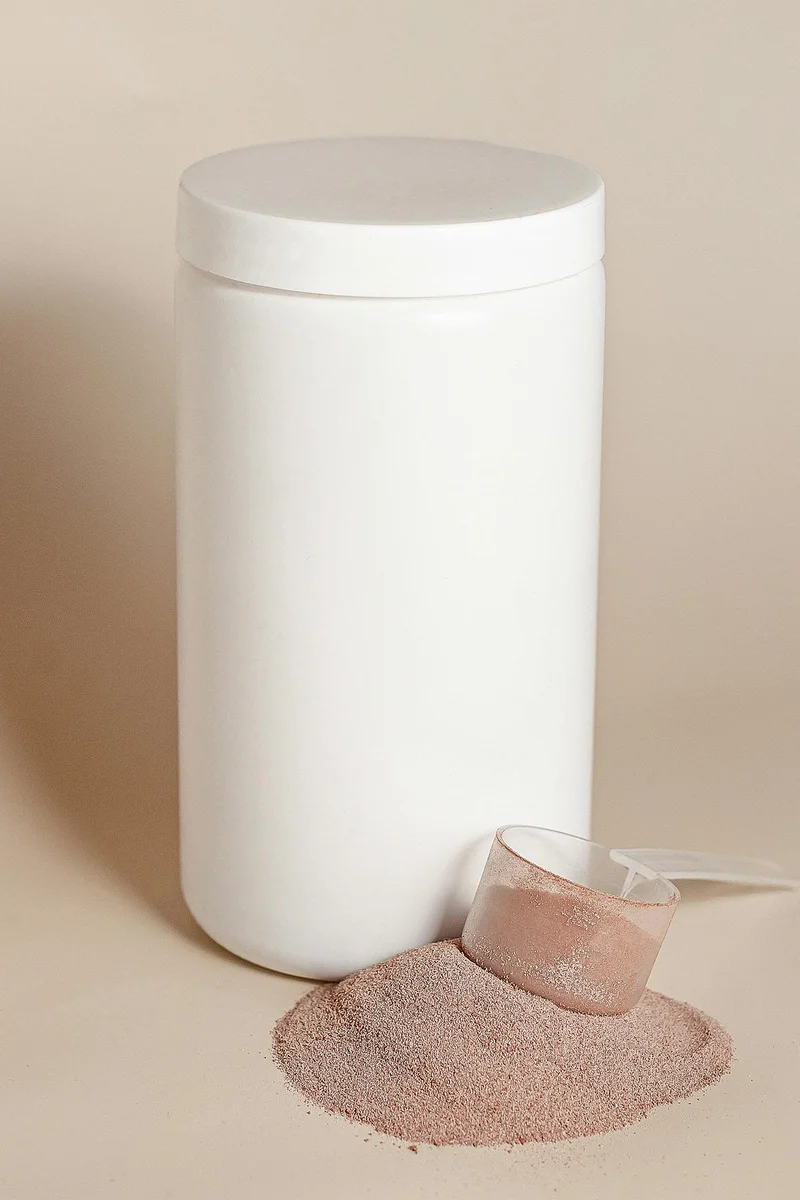 White protein powder jar with a scoop and spilled powder on a beige background representing casein and whey supplements